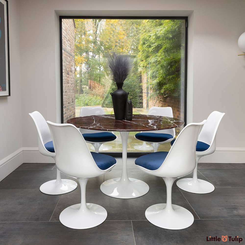 In the natural light sits this 120 levanto rosso Saarinan round dining table and 6 Tulip side chairs with blue cushions