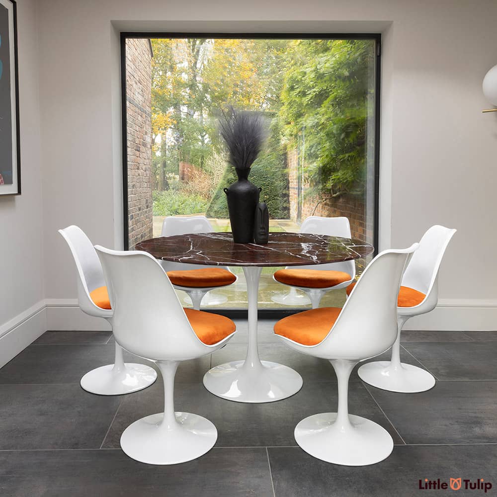 In the natural light sits this 120 levanto rosso Saarinan round dining table and 6 Tulip side chairs with orange cushions
