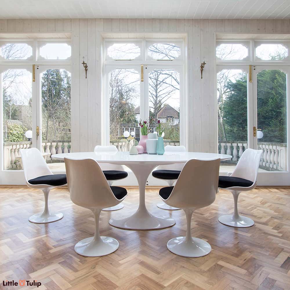 A dining space filled with natural light, feeling even more spacious with the white laminate oval 200 cm Tulip table, six chairs with space black cushions