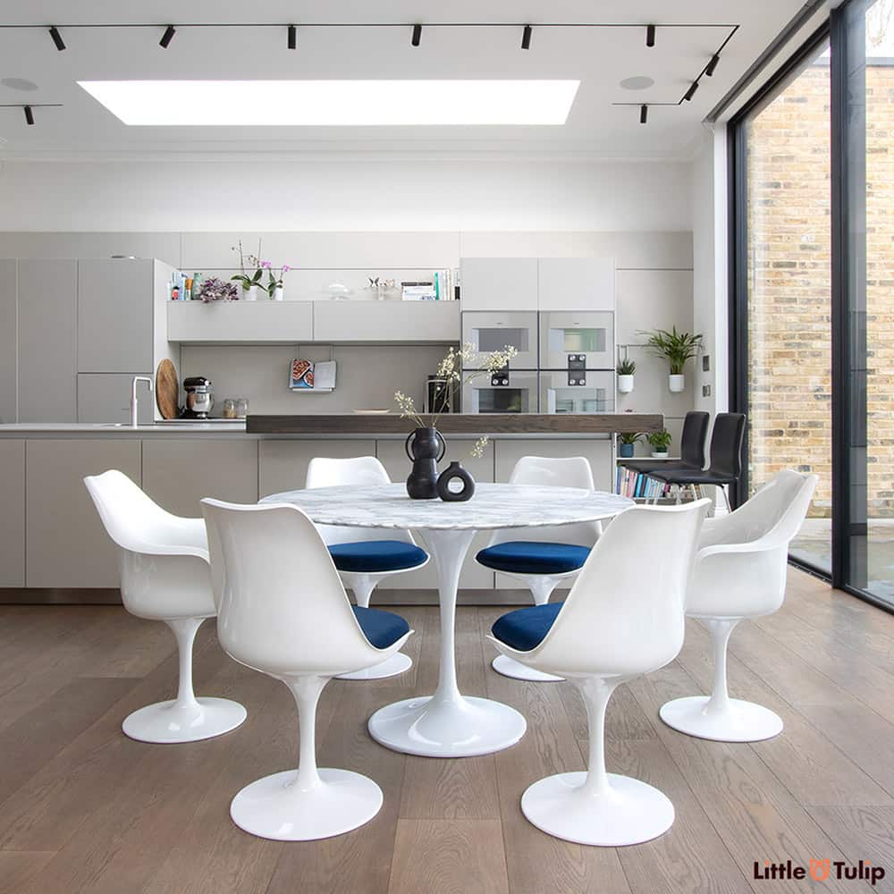 Set within a modern kitchen extension, four tulip side & 2 tulip arm chairs with blue pads sit next to the wonderful 120 cm round Arabescato Marble table