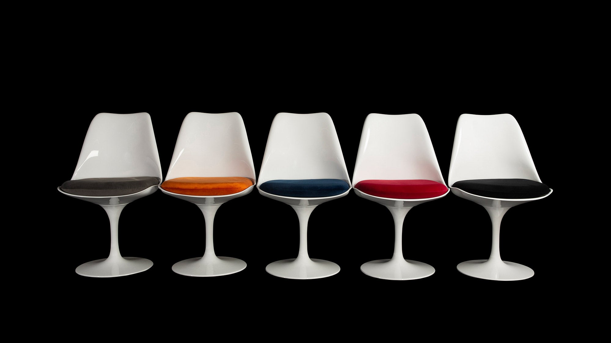 Like ducks in a row, a line of beautiful Eero Saarinen Tulip chairs stand out in white against the black background & each with a different cushion colour