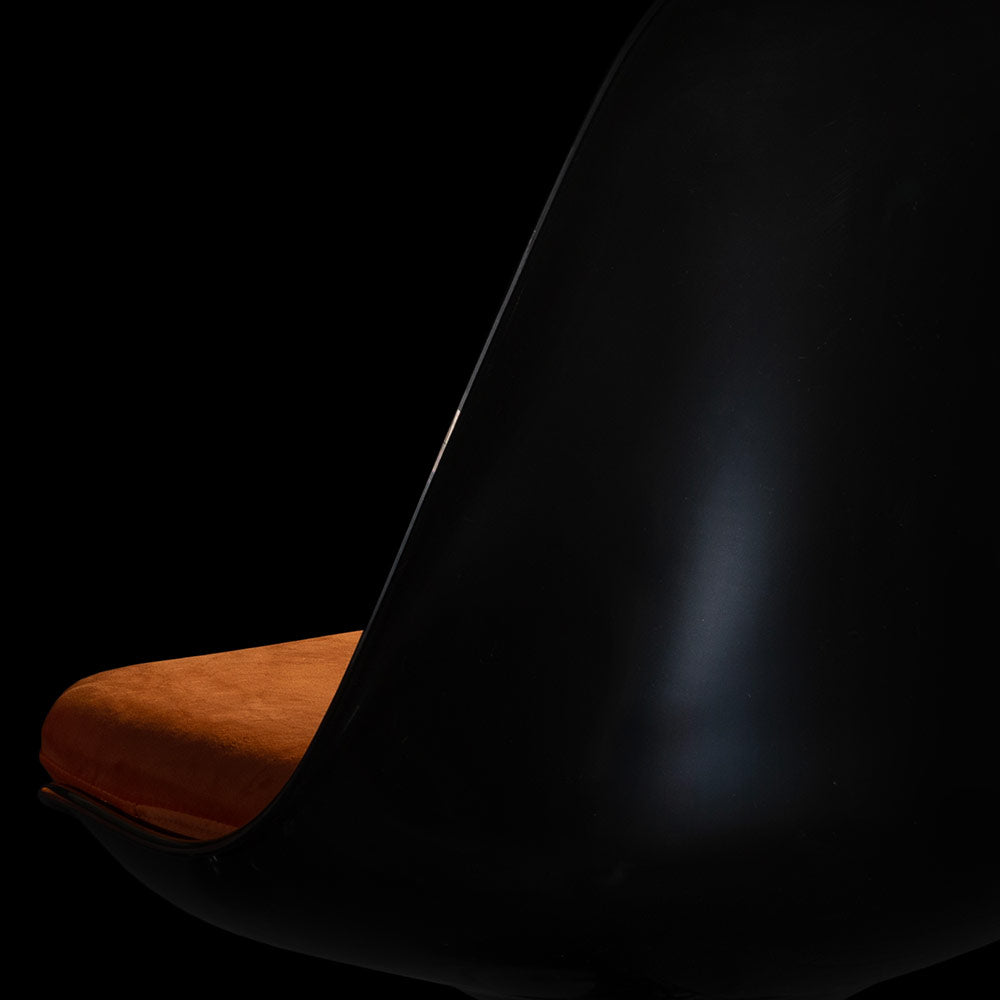 Pictured from the rear, an artistic dark and mysterious view of the Black Tulip Side Chair with a contrasting orange cushion with mood lighting