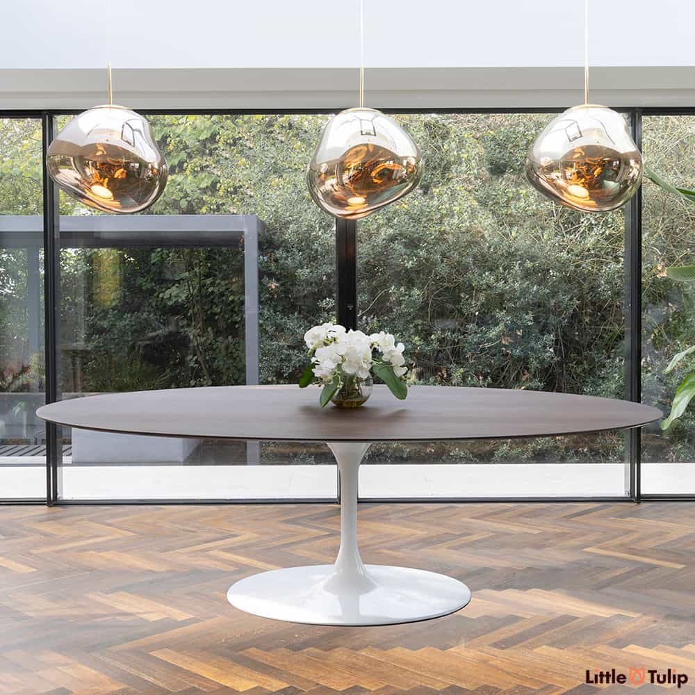 Set within a purpose built dining area, the largest 244 cm oval Tulip Dining table with a Walnut veneer top is seen underneath 3 hanging copper lights