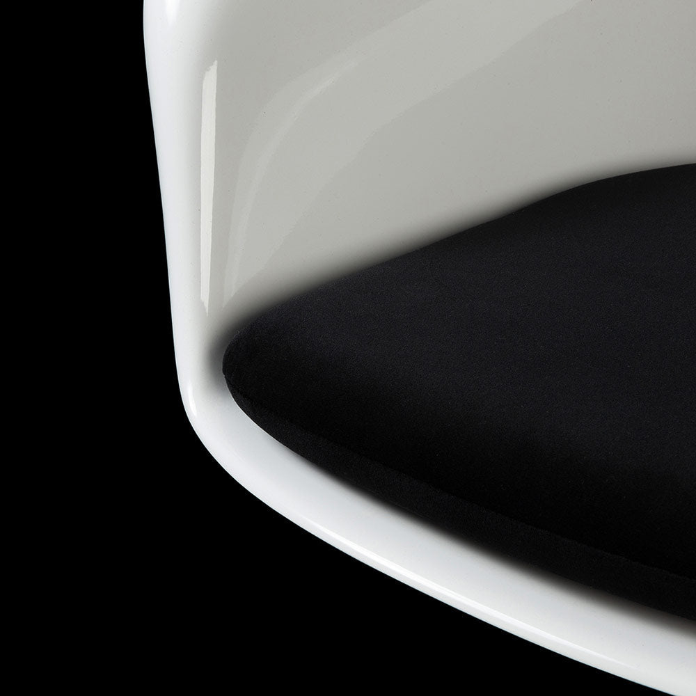 The encapsuled seat top of a Tulip Dining Arm Chair is seen in a glimmering white with contrasting black cushion sat within and a black backdrop
