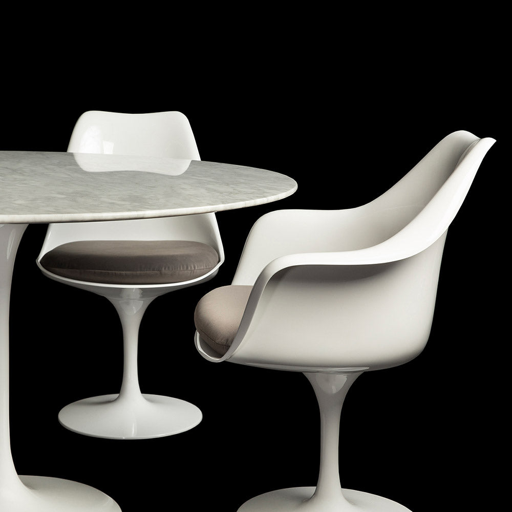 A Tulip Side & Arm Chair in white, one side and one front on, seen with so smooth grey cushions next to the 120 cm Arabescato Tulip Table in this set image