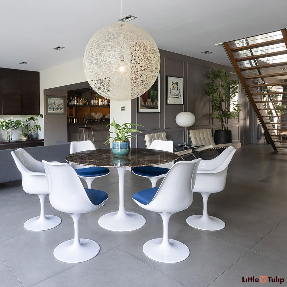 In the wide open plan space, a 120 emperador tulip table with 4 side, 2 arm chairs, and blue cushions sit centre stage