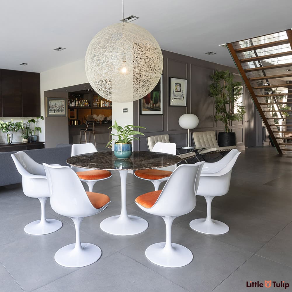 In the wide open plan space, a 120 emperador tulip table with 4 side, 2 arm chairs, and orange cushions sit centre stage