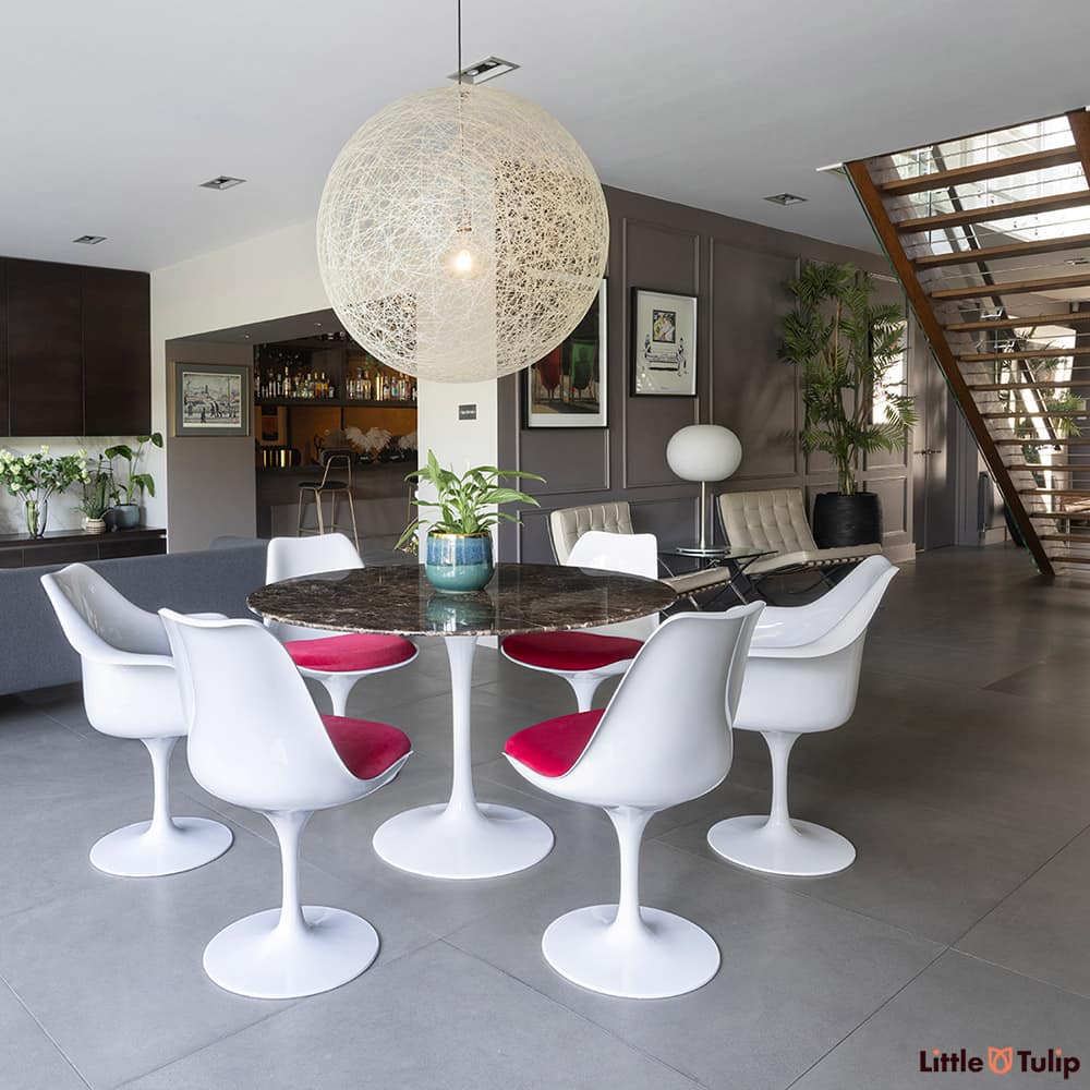 In the wide open plan space, a 120 emperador tulip table with 4 side, 2 arm chairs, and red cushions sit centre stage