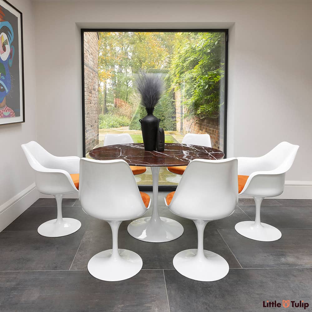 2 Tulip arms, 4 side chairs with orange cushion and a 120cm round levanto rosso Saarinen dining table glow in natural light