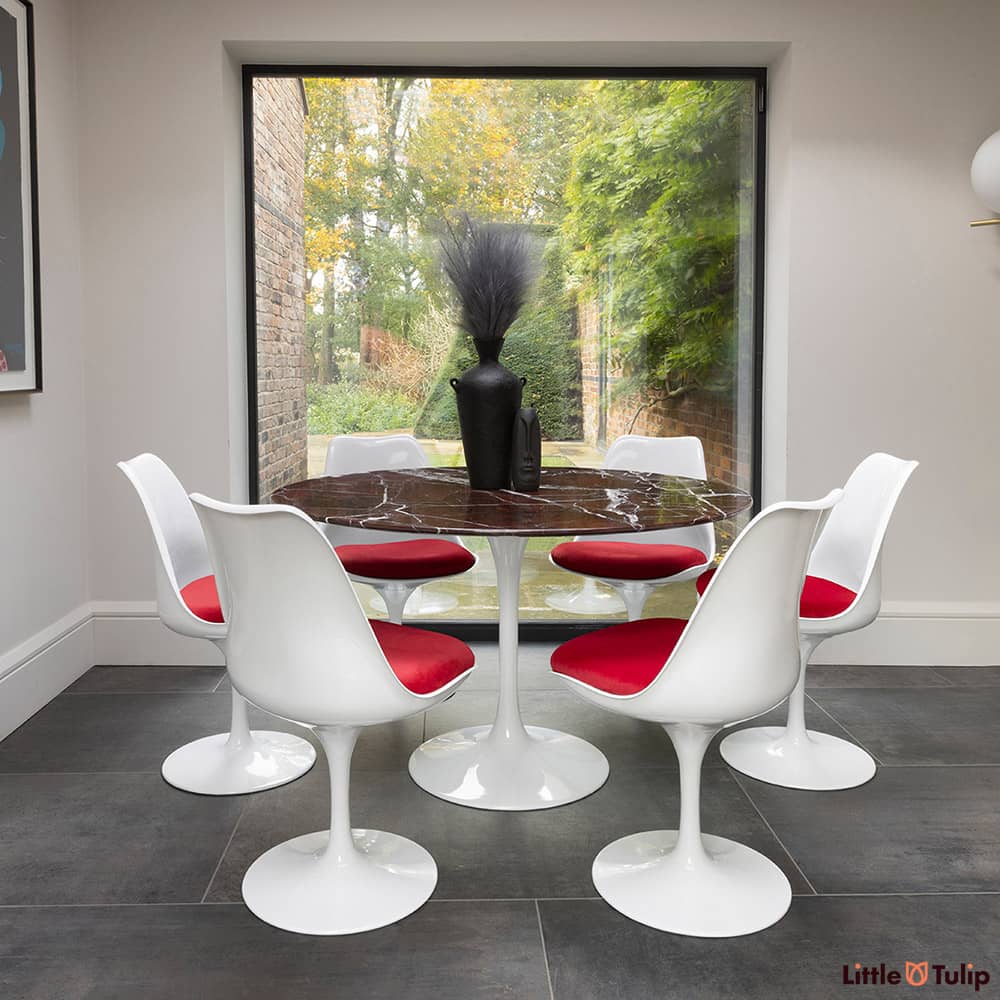 In the natural light sits this 120 levanto rosso Saarinan round dining table and 6 Tulip side chairs with red cushions