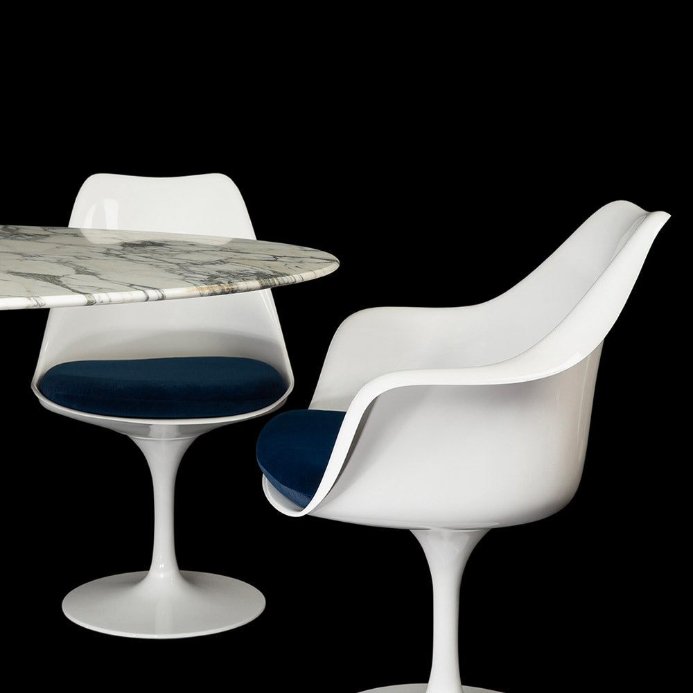 A Tulip Side & Arm Chair in white, one side and one front on, seen with so sapphire blue cushions next to a 170 cm Arabescato Tulip Table in this set image