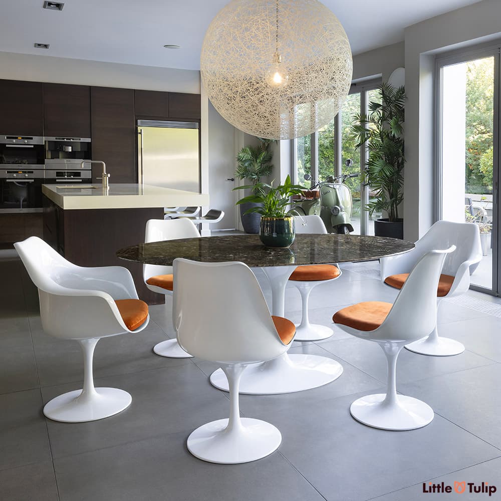 In natural light the 170 Emperador Tulip table, 4 side, 2 arm chairs with orange cushions under an amazing ceiling light
