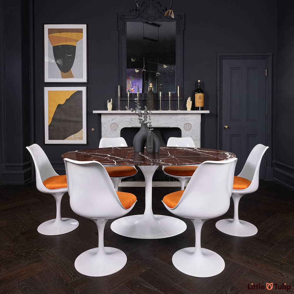 170 levanto rosso Saarinen oval dining table and 6 Tulip side chairs and orange cushions add colour to this dark-themed room