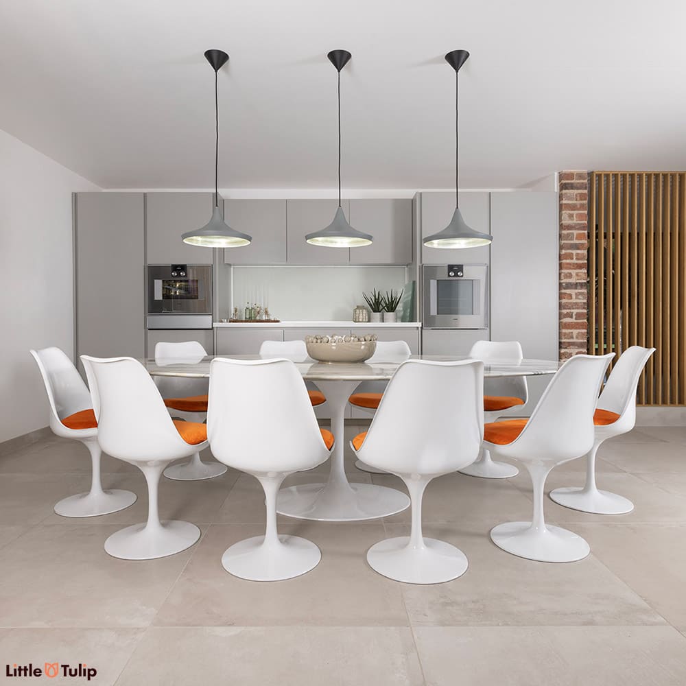 10 white Tulip side chairs and orange cushions surround this gorgeous Arabescato Tulip dining table in a bright, airy kitchen
