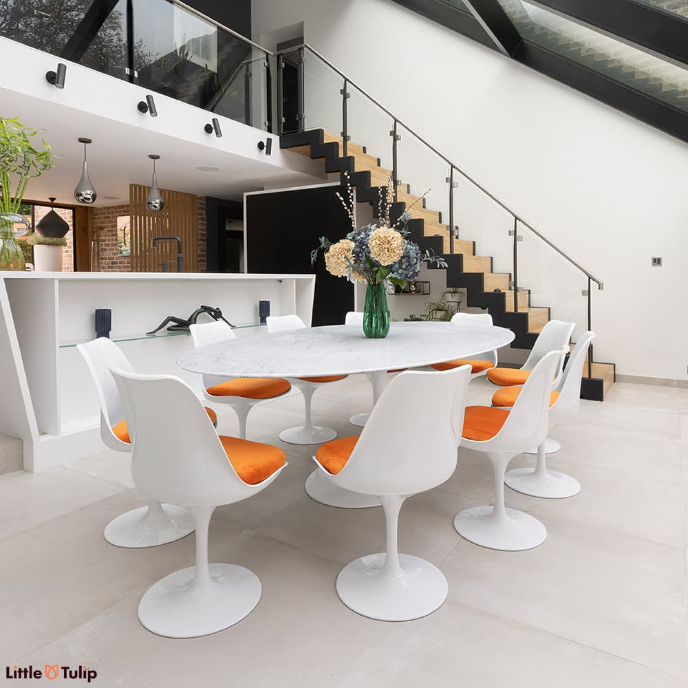The classic look, a carrara marble Tulip Table and 10 Tulip chairs and orange cushions flatters the contemporary dining space