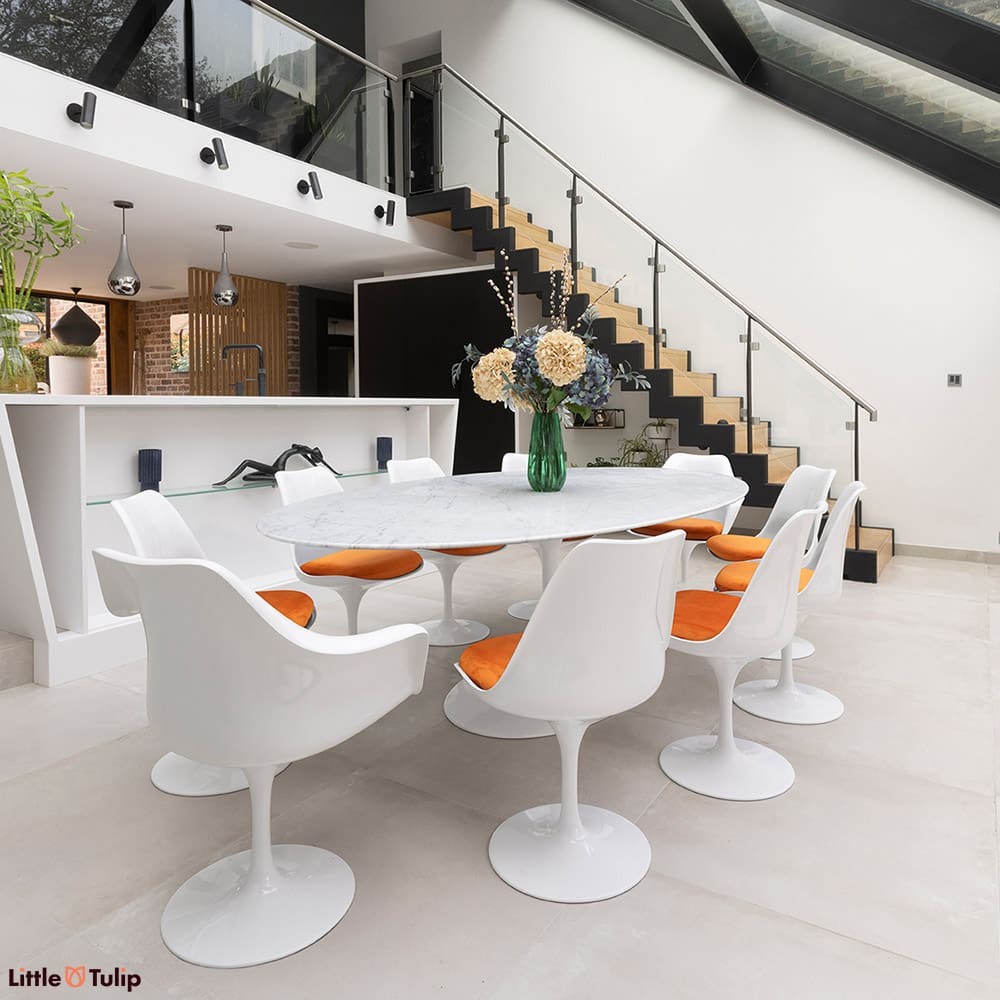The perfect dining scene, a carrara marble Tulip table and 8 side and 2 Tulip arm chairs and orange cushions on a tiled floor