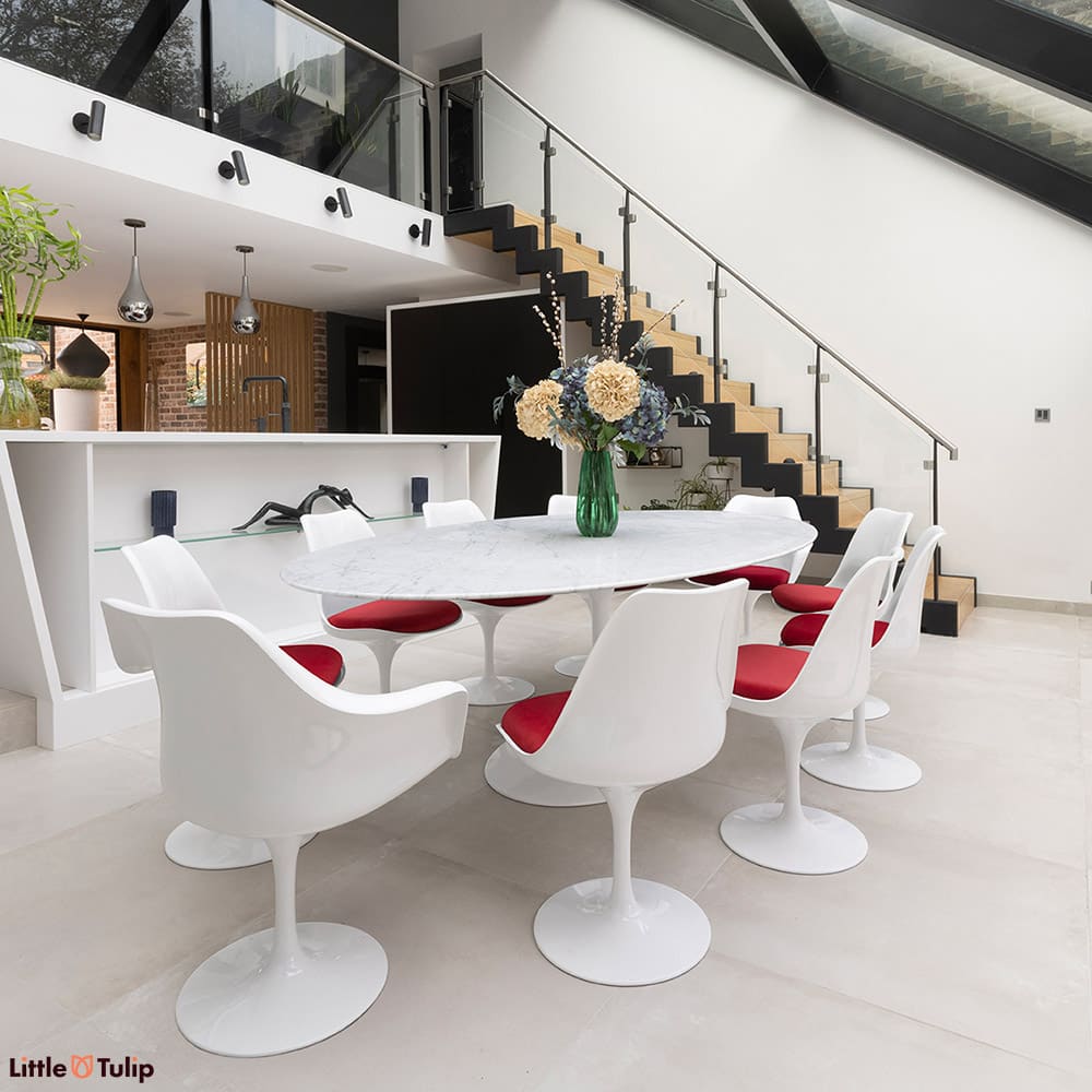 The perfect dining scene, a carrara marble Tulip table with 8 side and 2 Tulip arm chairs and red cushions on a tiled floor