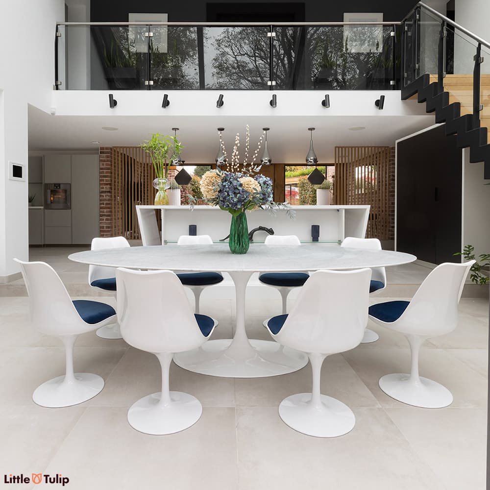 In a fresh kitchen, a bright white Carrara marble Tulip table, 8 chairs with blue cushions astound.