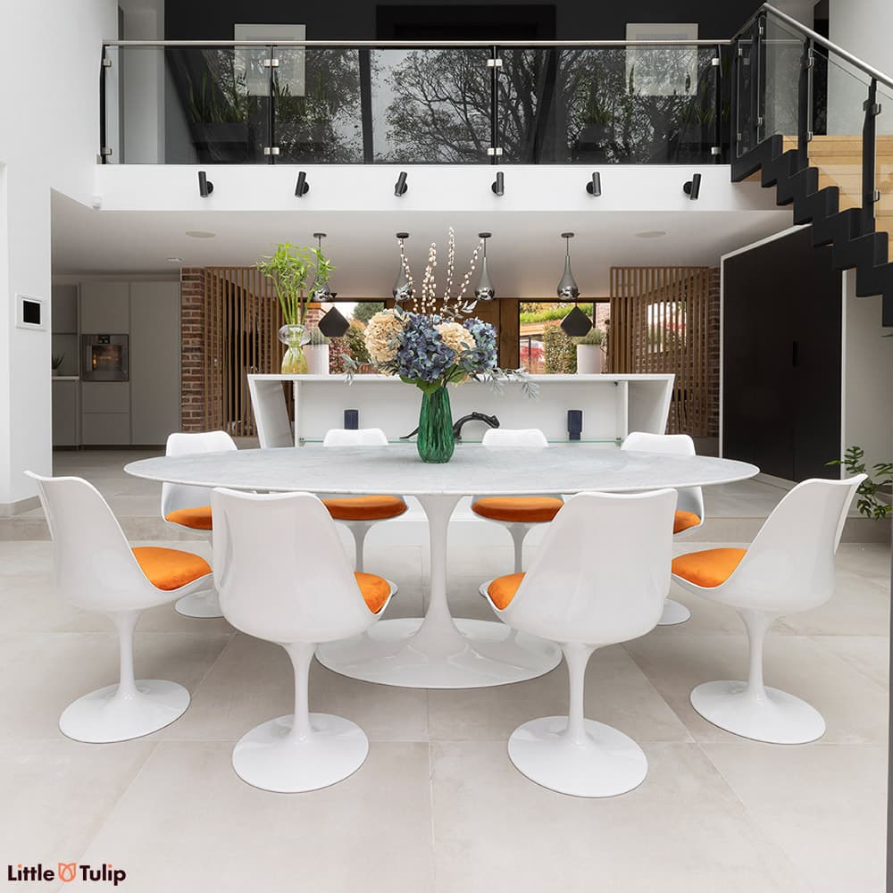 In a fresh kitchen, a bright white Carrara marble Tulip table, 8 chairs with orange cushions astound.