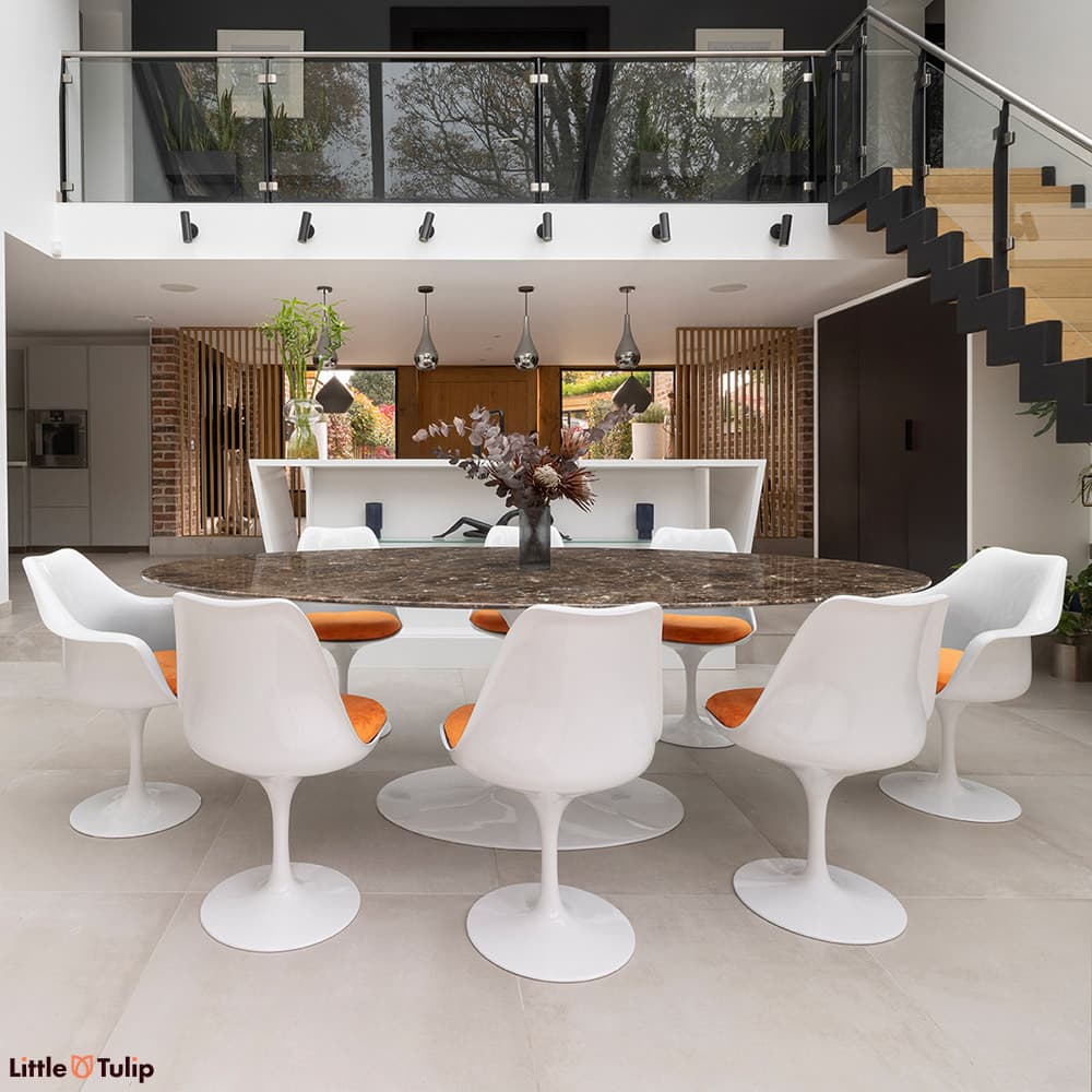 An eye-catching 244 Emperador Tulip table with 6 side, 2 arm chairs and orange cushions in a modern open-plan kitchen