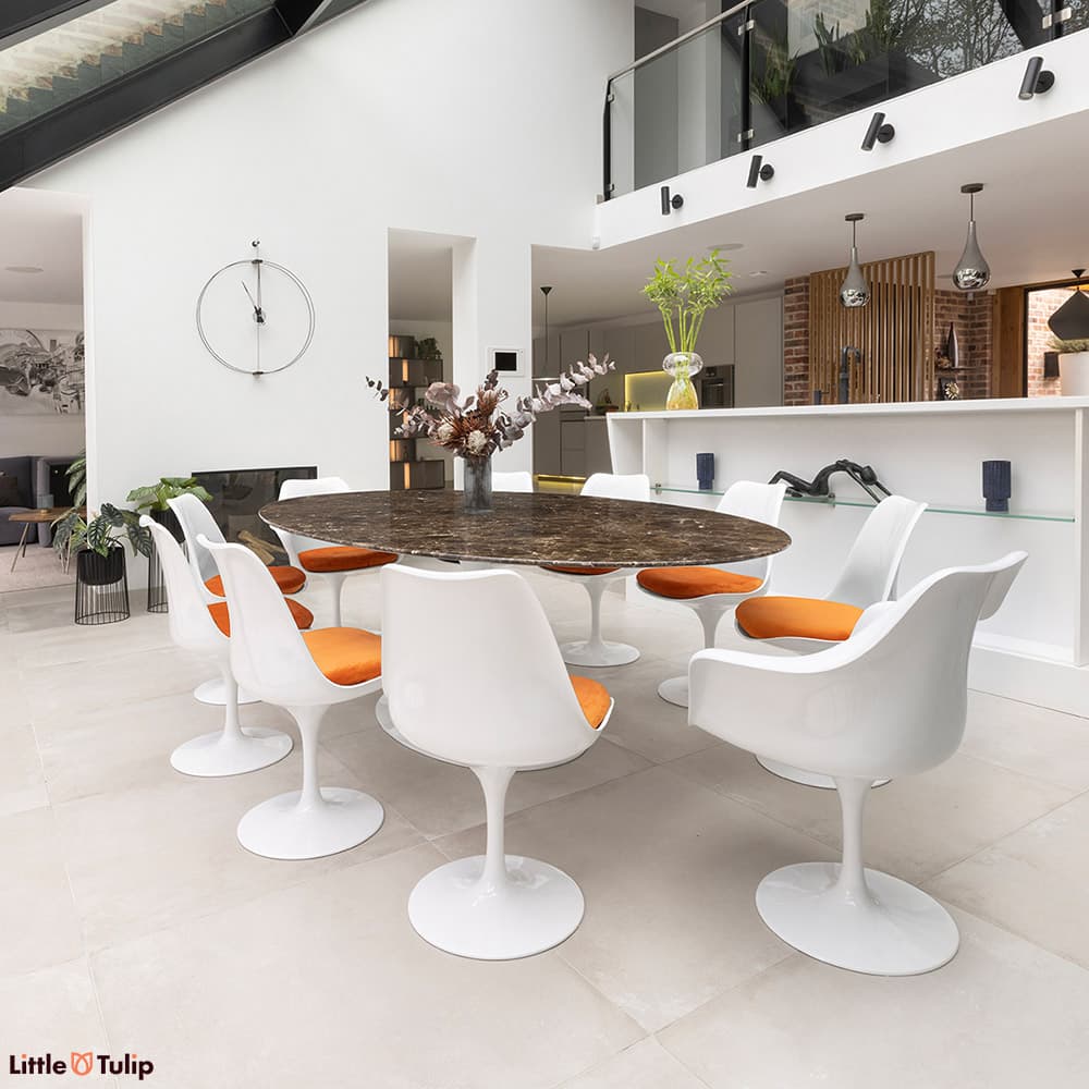 This luxurious emperador 244 tulip table with 8 side and 2 arm chairs with orange cushions enriches this all-white kitchen