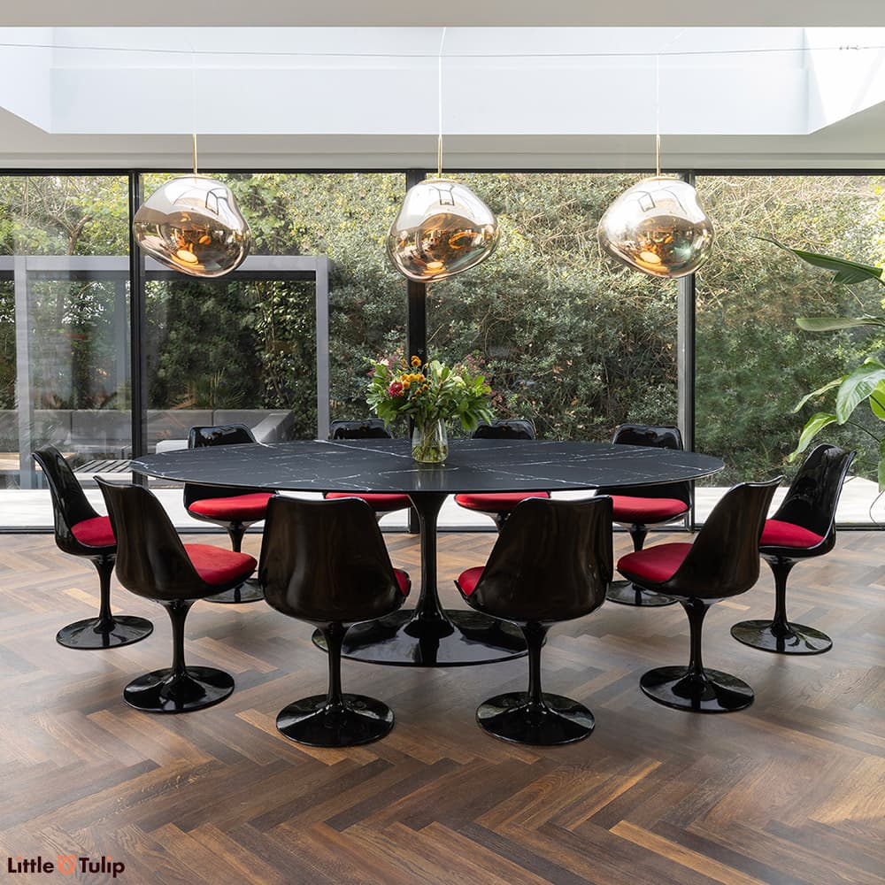 In a complimentary dark themed dining space sits a neromarquina Tulip Table with 10 black Tulip side chairs with red cushions