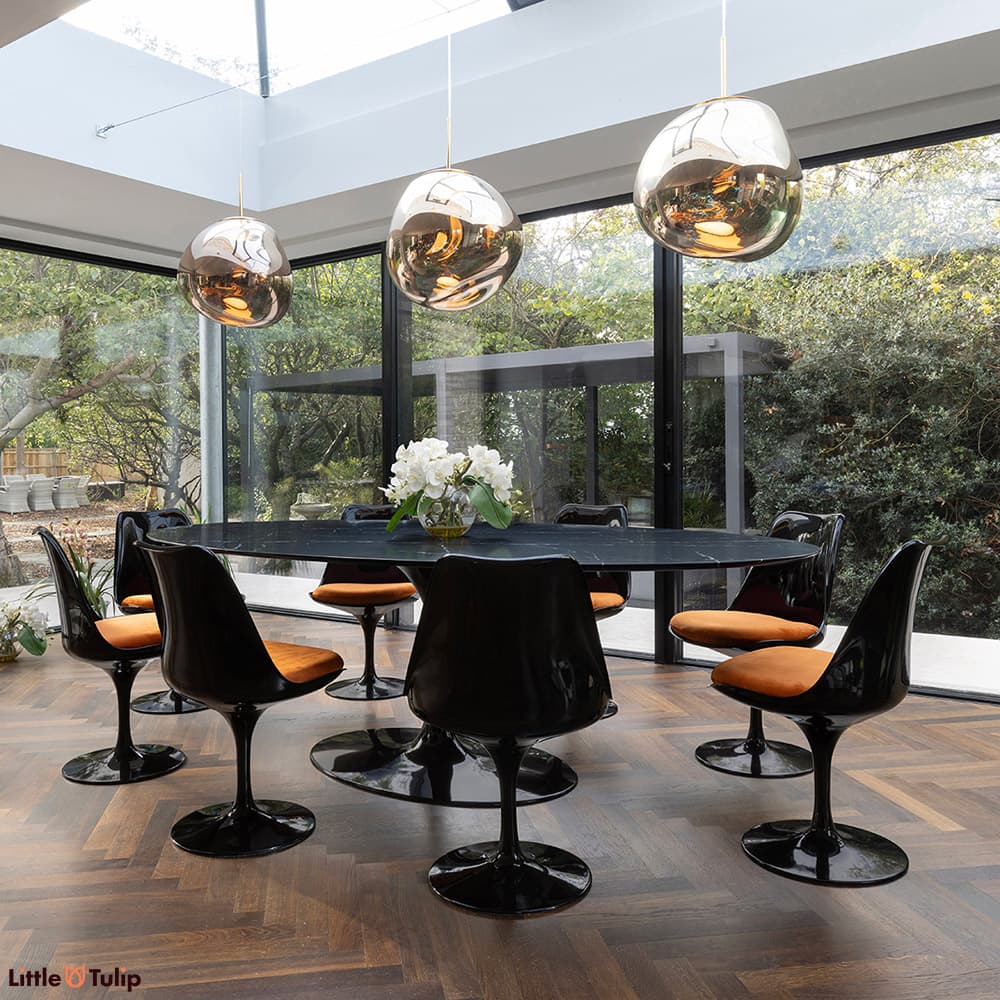 A stunning all black 244 Tulip Table with 8 side chairs and orange cushions displayed here in a well-lit natural floor space
