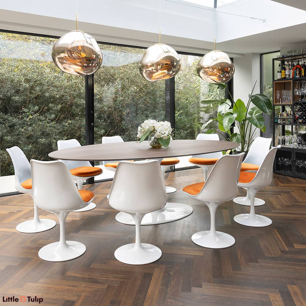 This Saarinen Tulip Dining Table in walnut with 10 white Tulip chairs with orange cushions is sat in a beautiful conservatory