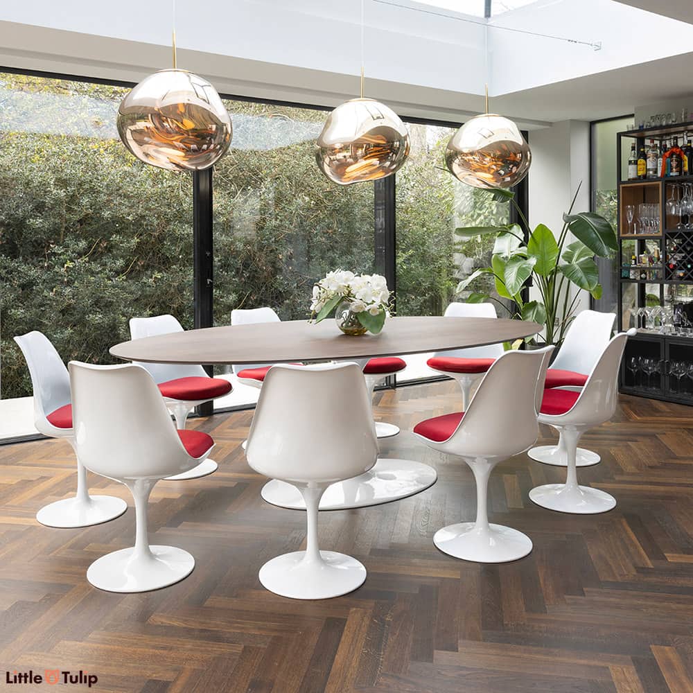 This Saarinen Tulip Dining Table in walnut with 10 white Tulip chairs with red cushions is sat in a beautiful conservatory