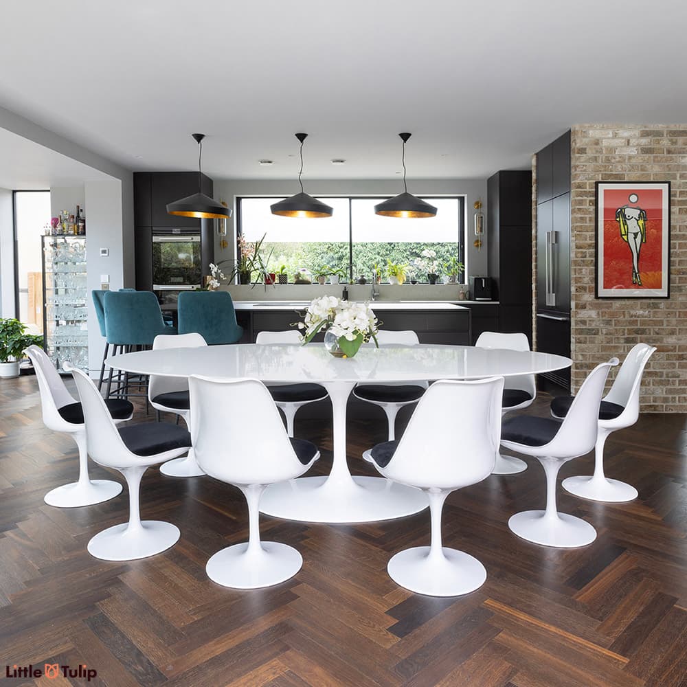A white laminate Saarinen Tulip Dining Table with 10 white Tulip chairs with black cushions in a stylish kitchen dining space