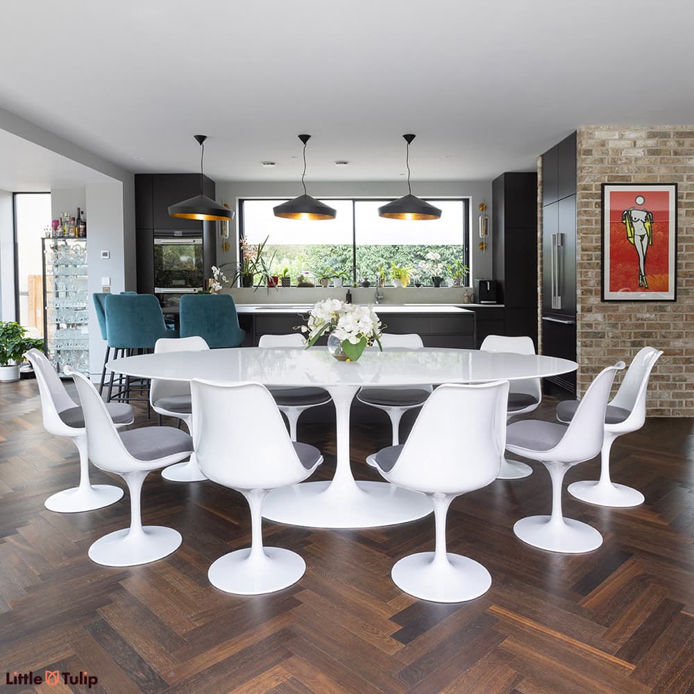A white laminate Saarinen Tulip Dining Table with 10 white Tulip chairs with grey cushions in a stylish kitchen dining space