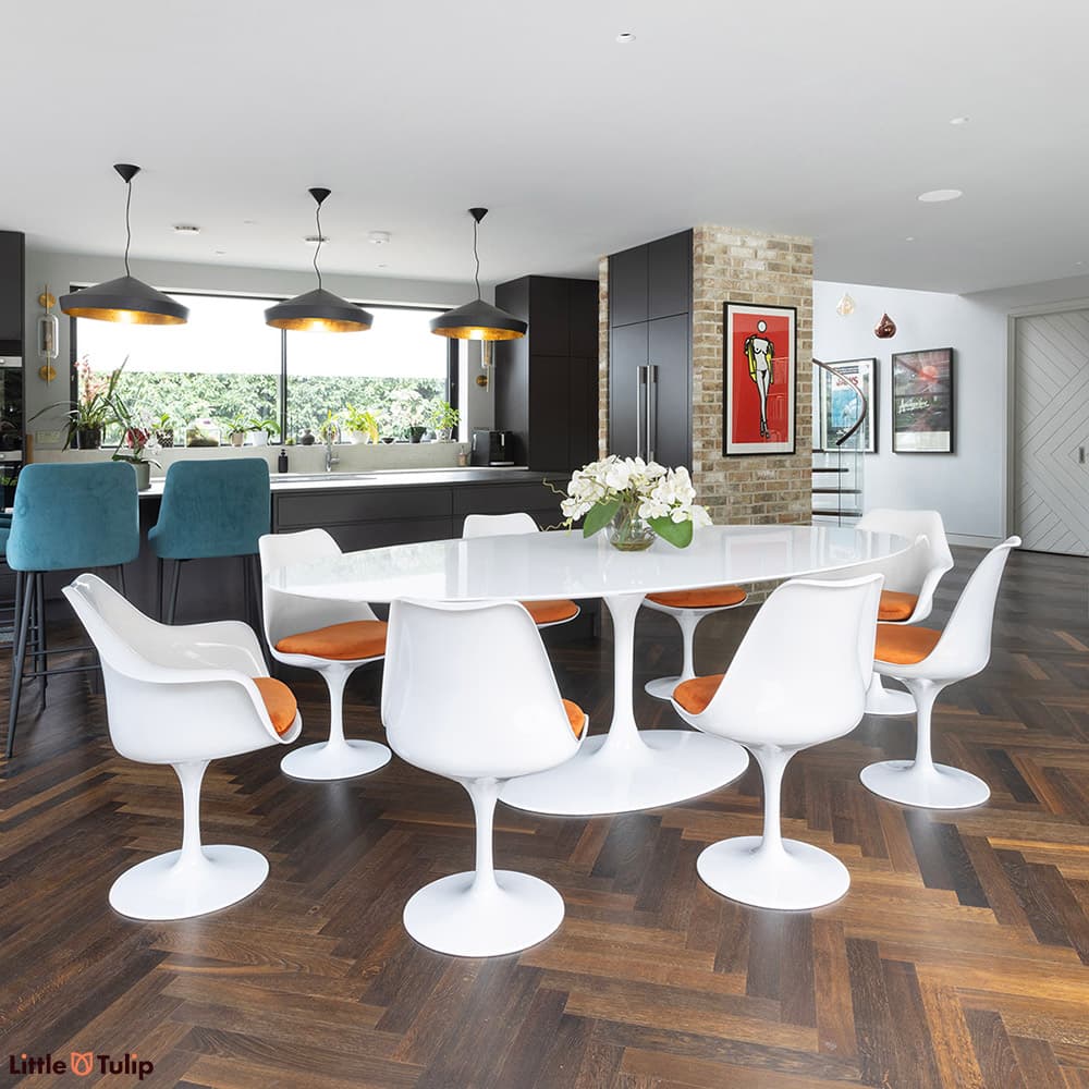 A white laminate 244 Tulip Table and its 6 side, 2 arm chairs orange cushions brightens this dark themed contemporary space
