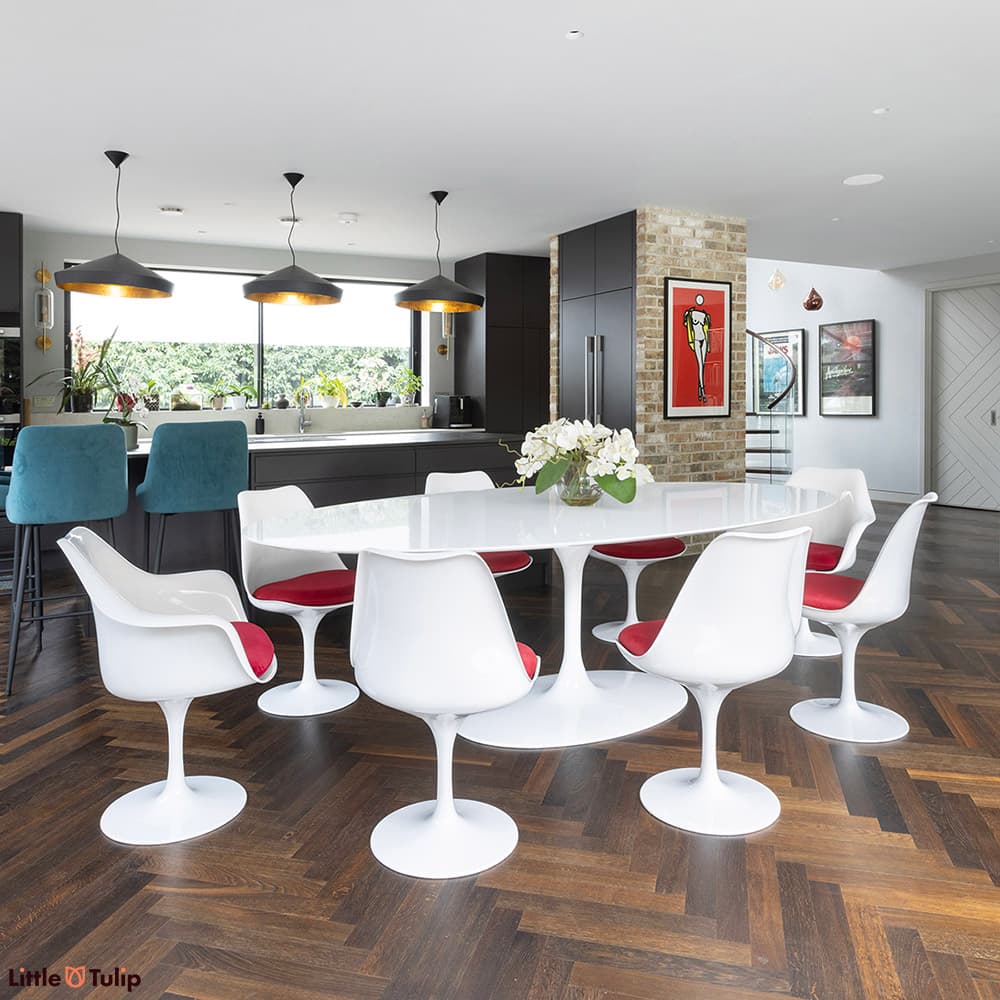 A white laminate 244 Tulip Table and its 6 side, 2 arm chairs red cushions brightens this dark themed contemporary space