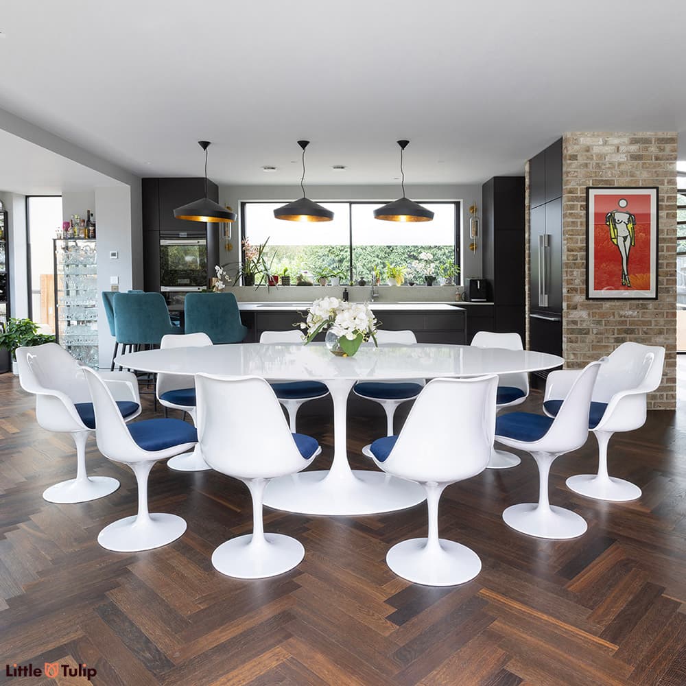 The largest white laminate Saarinen tulip table, 8 side chairs, 2 arm chairs and blue cushions excel on a herringbone floor
