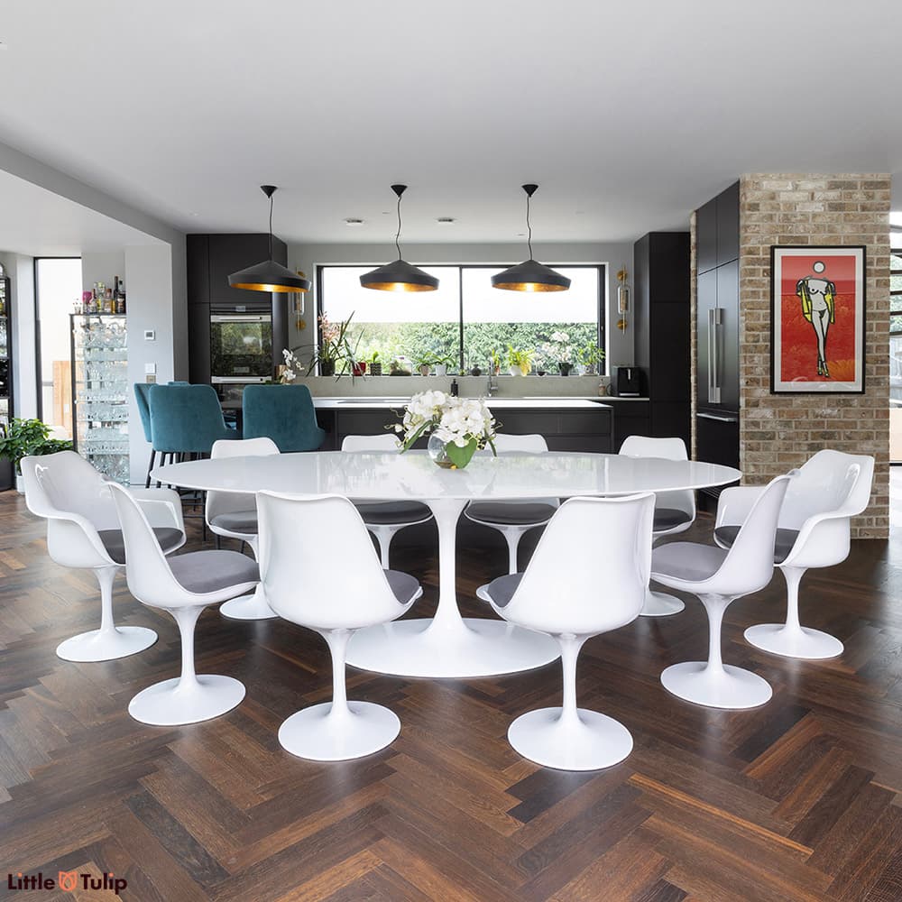 The largest white laminate Saarinen tulip table, 8 side chairs, 2 arm chairs and grey cushions excel on a herringbone floor