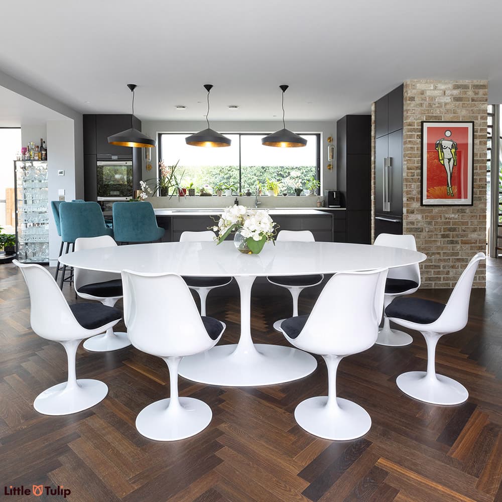 In a modern, dark-themed kitchen, a 244 white laminate Tulip table and 8 chairs with black cushions bring brightness