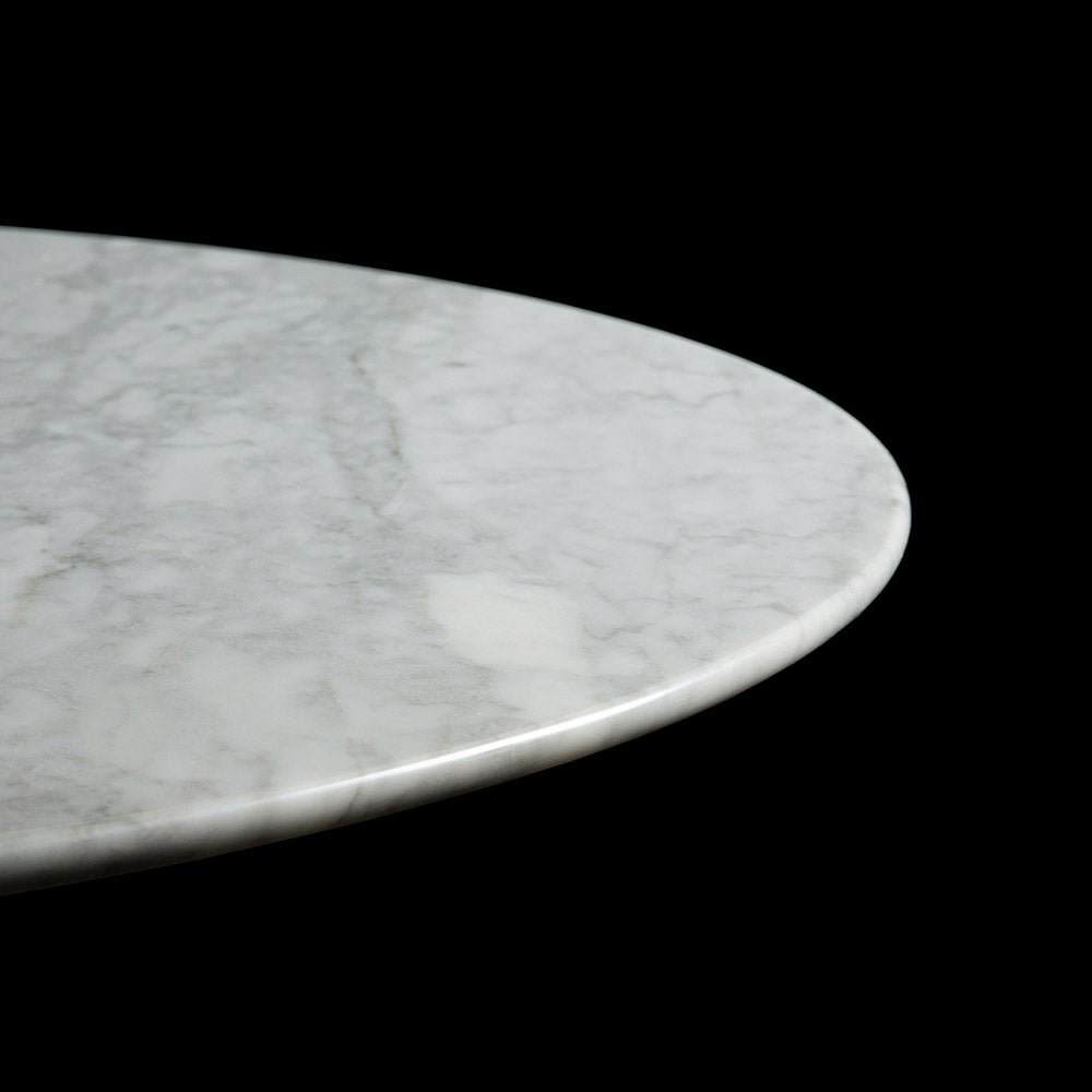 A striking image showing part of a circular Tulip Table in white Carrara Marble against a black backdrop, with the beveled edging and natural top veining