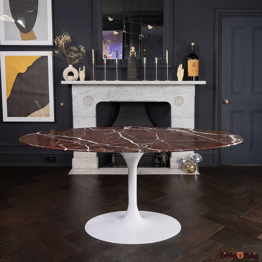 Standing in the front of a white marble fireplace in a dark dining space is the 170 Saarinen levanto rosso oval dining table