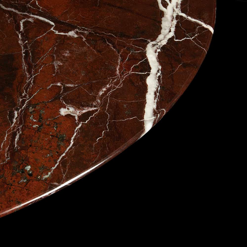 Against a black background, the side & edging of a Levanto Rosso marble table is seen with its shimmering red hue & various white quartz veins throughout