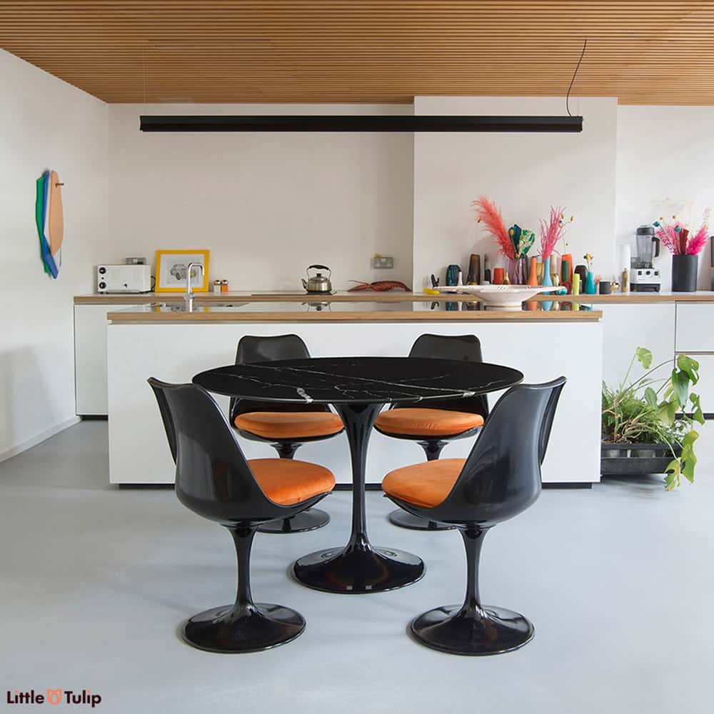 A 120 cm Tulip Table that makes a dark & powerful statement with the rich Nero Marquina black marble along with four Tulip Side Chairs & Orange cushions