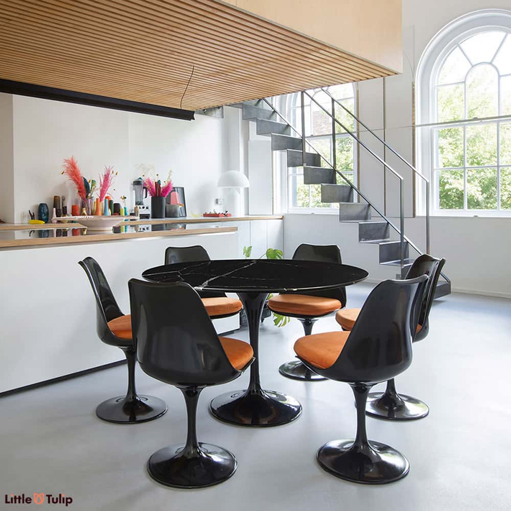 A dining set that brings out dark tones in fine style, encompassing a Nero Marquina Black Marble Tulip Dining Table with six side chairs in orange cushions