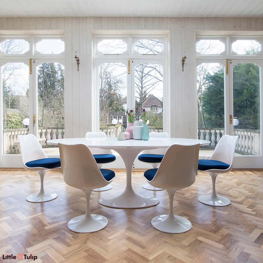 A dining space filled with natural light, feeling even more spacious with the white laminate oval 200 cm Tulip table, six chairs with royal blue cushions