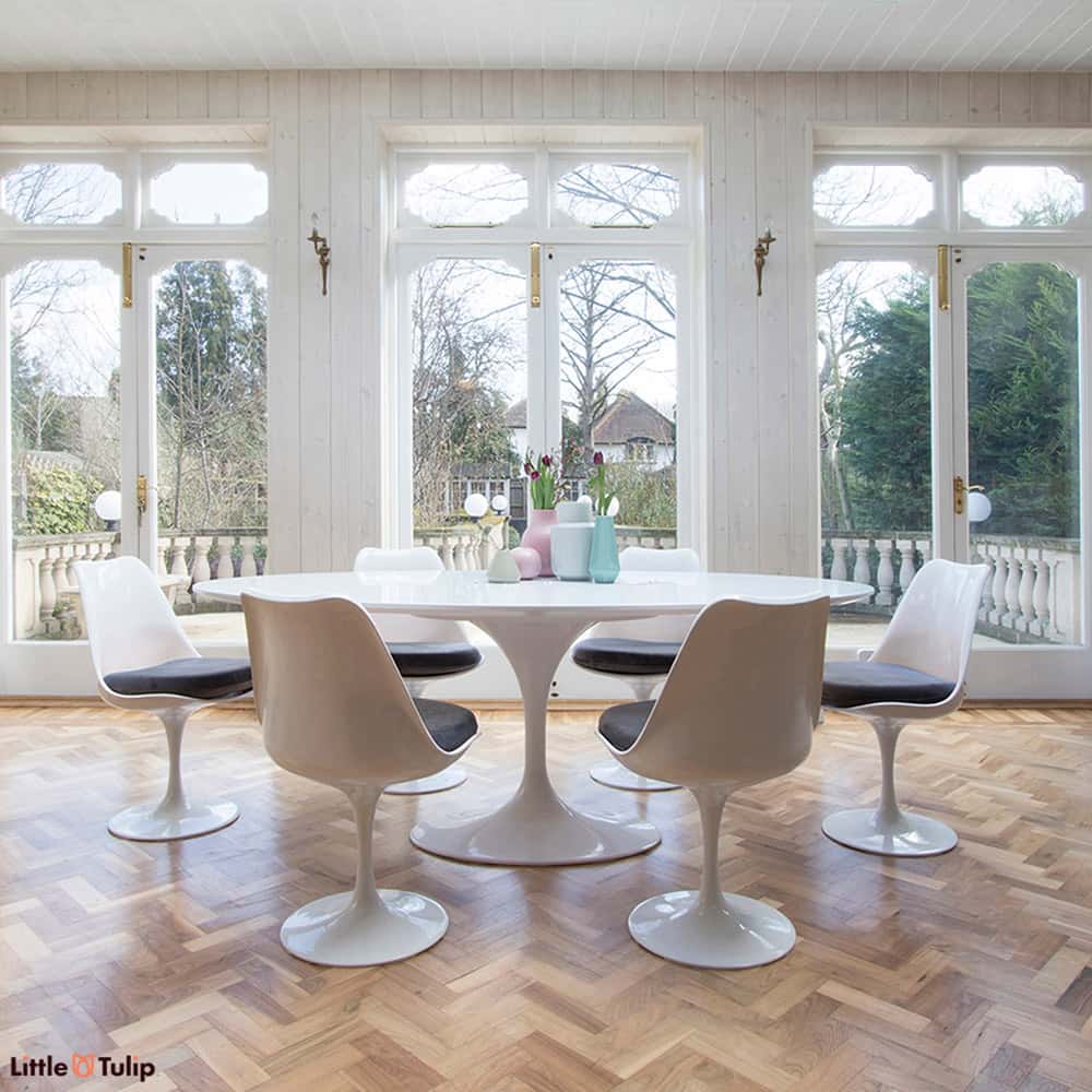 A dining space filled with natural light, feeling even more spacious with the white laminate oval 200 cm Tulip table, six chairs with marble grey cushions