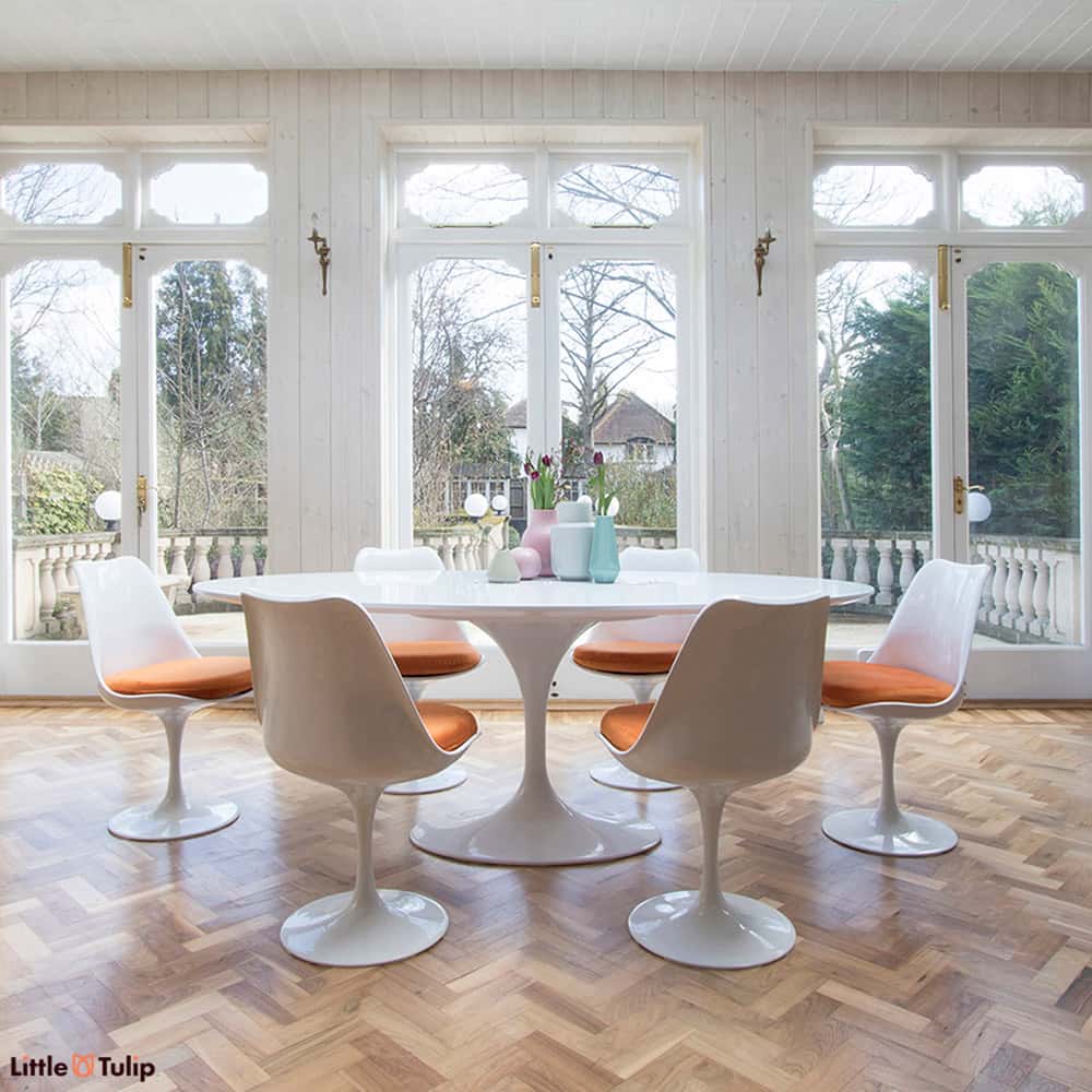 A dining space filled with natural light, feeling even more spacious with the white laminate oval 200 cm Tulip table, six chairs with vibrant orange cushions