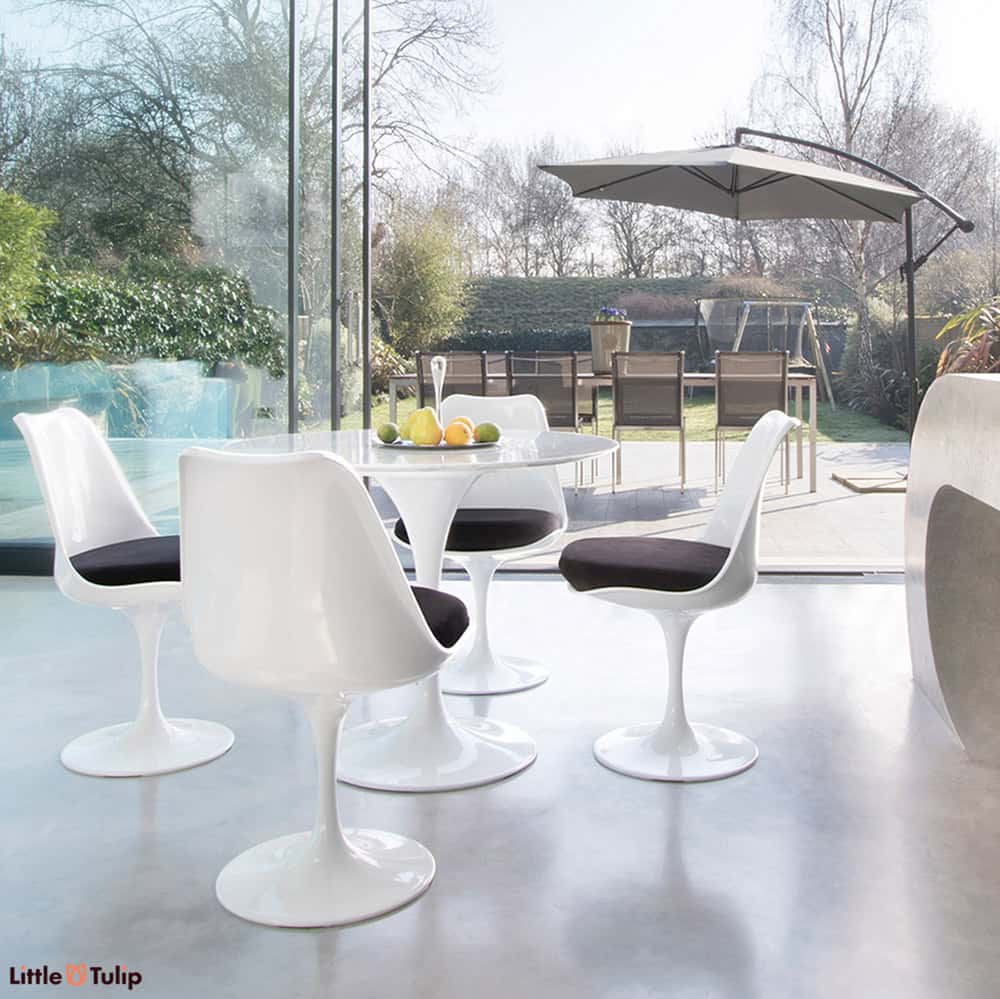 Within a modern kitchen and looking out to summer patio scene is the Carrara Marble 90cm Tulip Table with four side chairs with jet black cushion pads