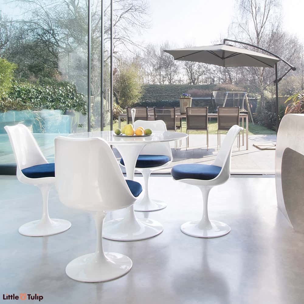 Within a modern kitchen and looking out to summer patio scene is the Carrara Marble 90cm Tulip Table with four side chairs with ocean blue cushion pads