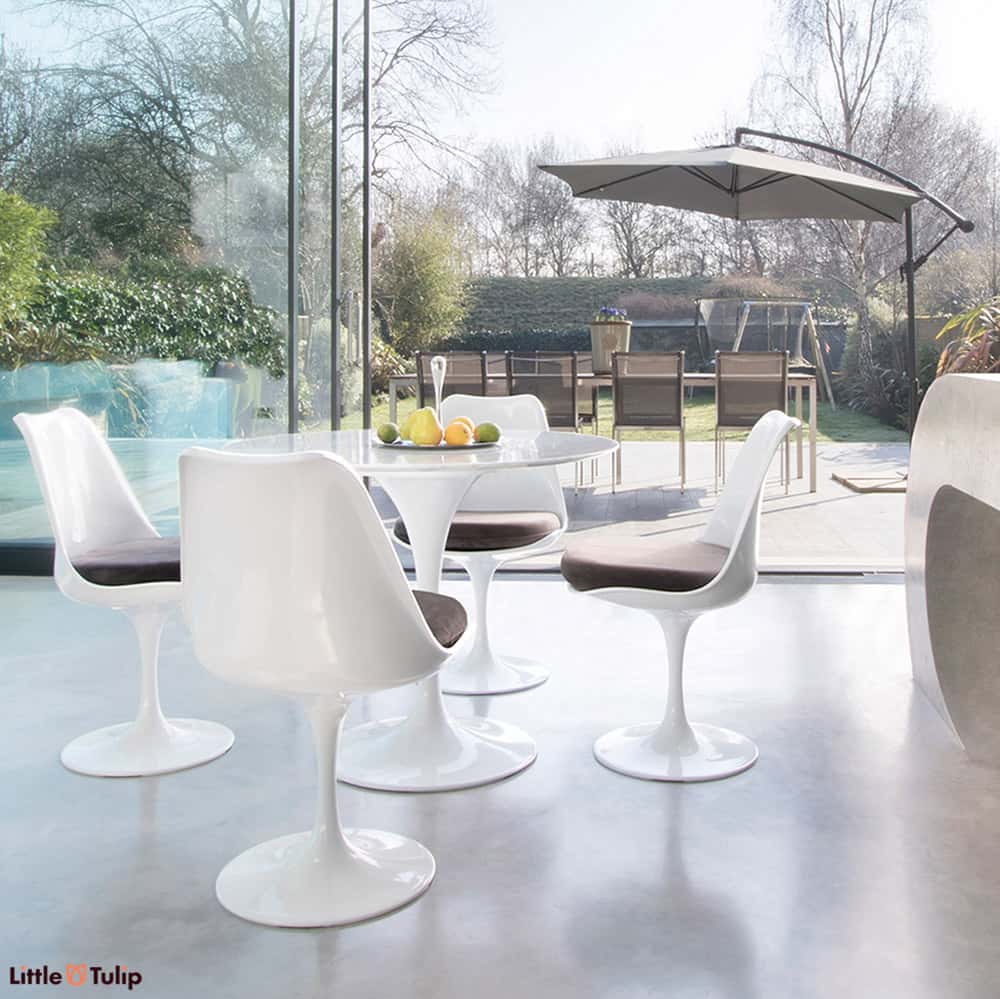 Within a modern kitchen and looking out to summer patio scene is the Carrara Marble 90cm Tulip Table with four side chairs with mid grey cushion pads