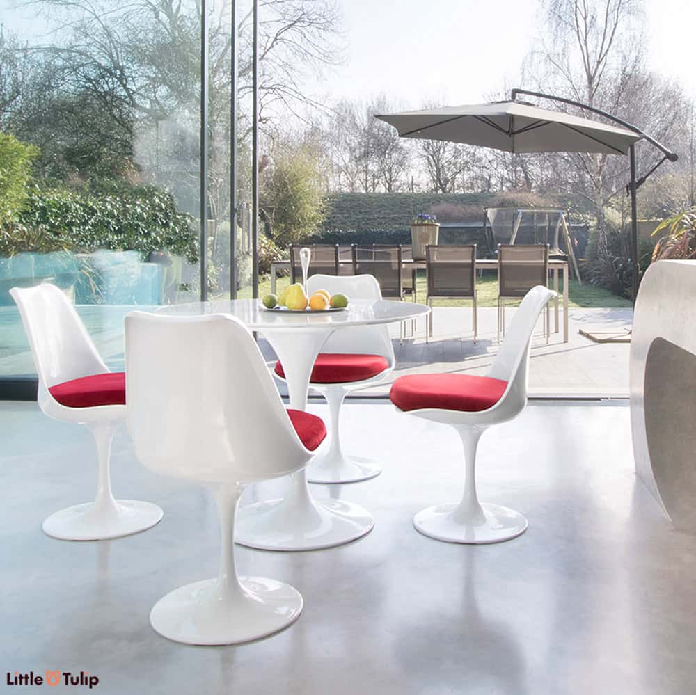 Within a modern kitchen and looking out to summer patio scene is the Carrara Marble 90cm Tulip Table with four side chairs with deep red cushion pads