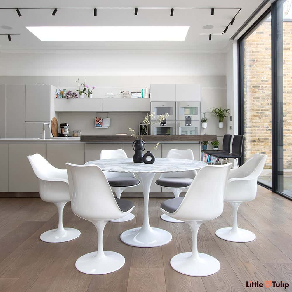 Set within a modern kitchen extension, four tulip side & 2 tulip arm chairs with grey pads sit next to the wonderful 120 cm round Arabescato Marble table