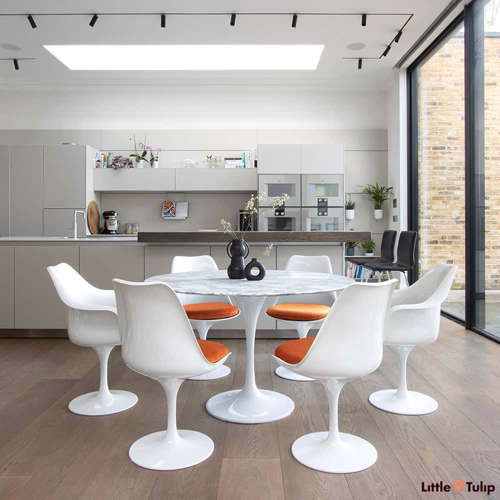 Set within a modern kitchen extension, four tulip side & 2 tulip arm chairs with orange pads sit next to the wonderful 120 cm round Arabescato Marble table